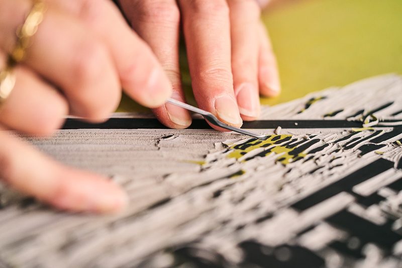 Close-up of hands carving fine lines into a lino block