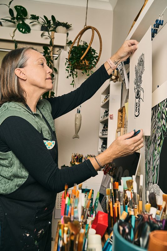 A printmaker hanging a fresh print on her studio wall above jars of brushes