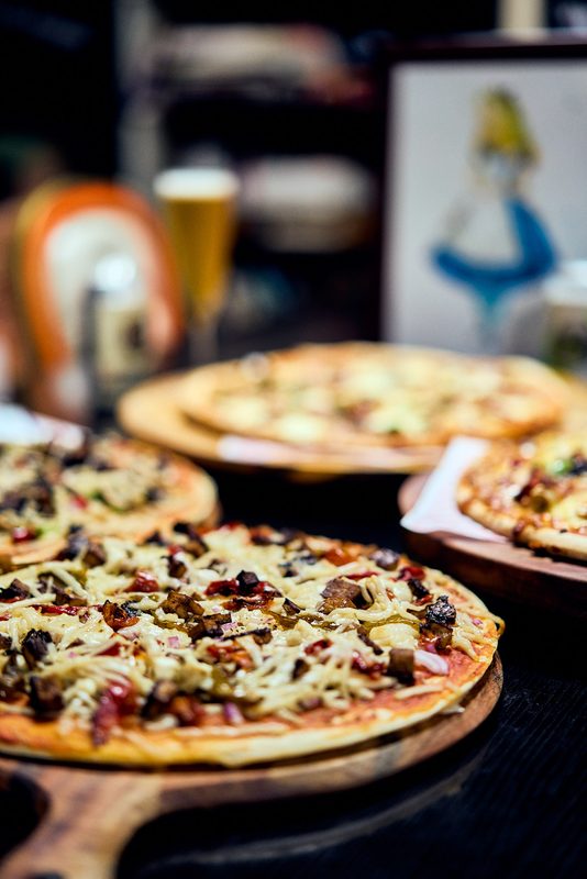 Three pizzas on wooden boards along a dark table, a beer and an illustrated print in the background